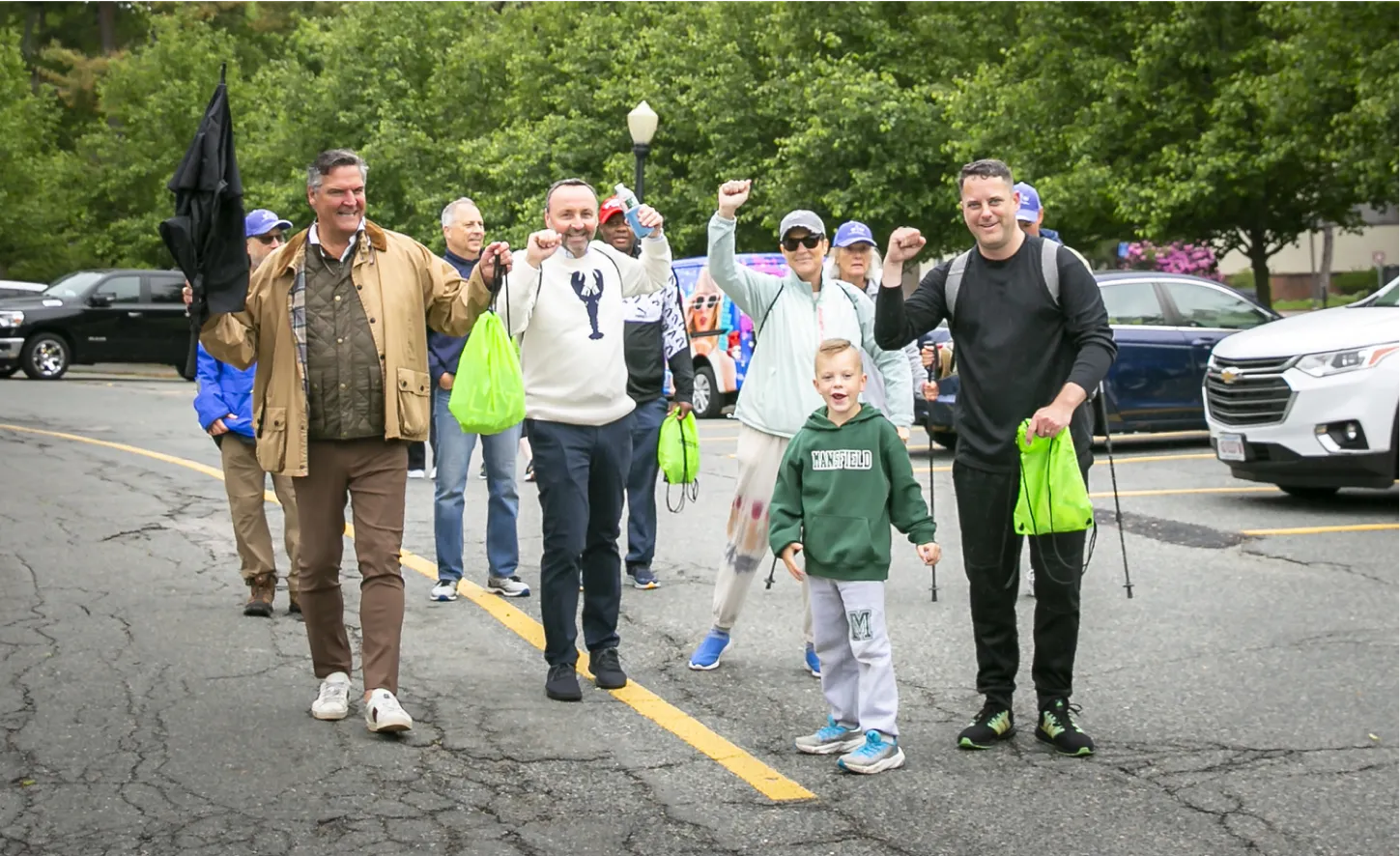 Enthusiastic group of people walking outdoors, holding green bags and raising their hands