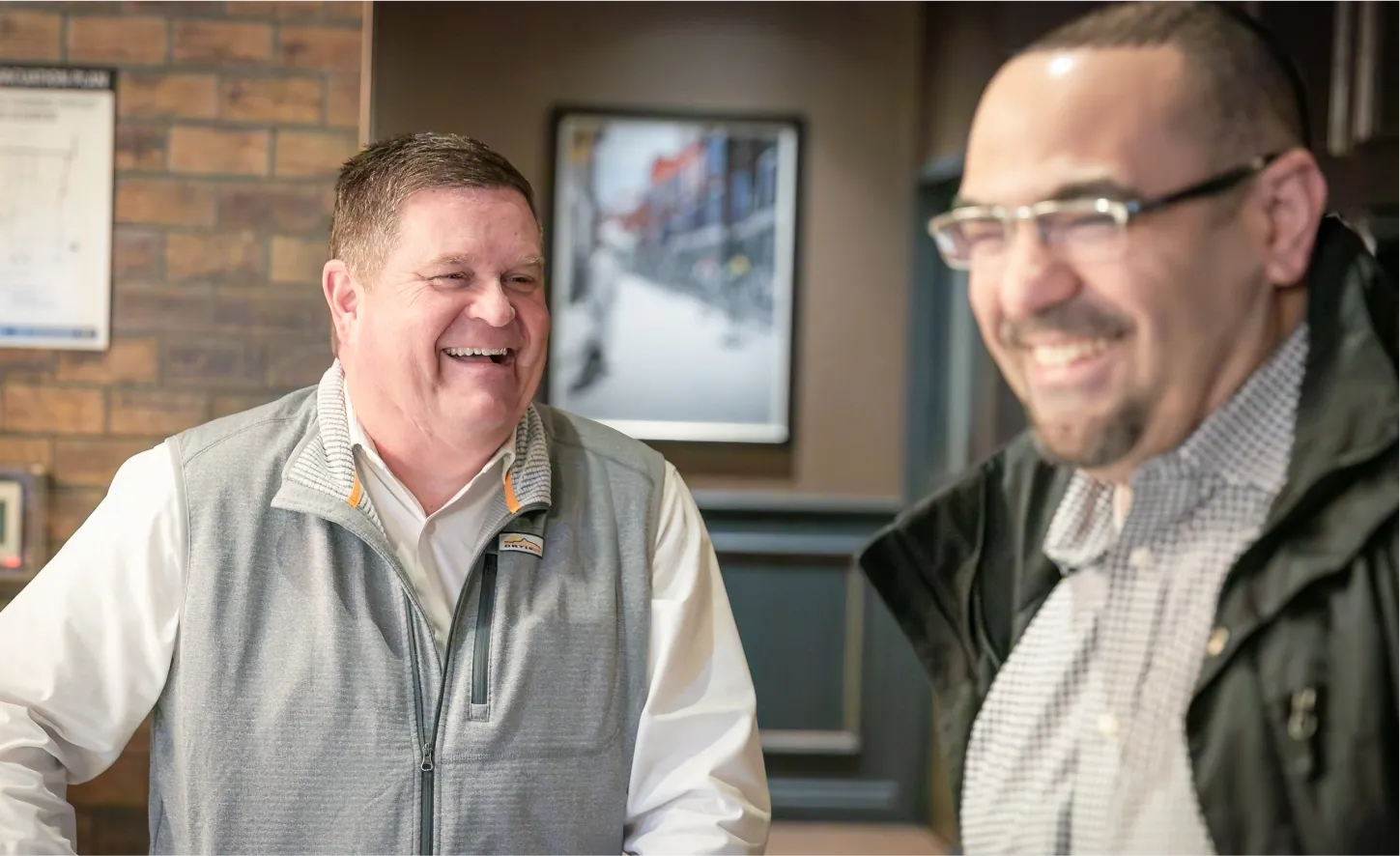 Two men share a laugh in a warmly lit business setting with a brick accent wall