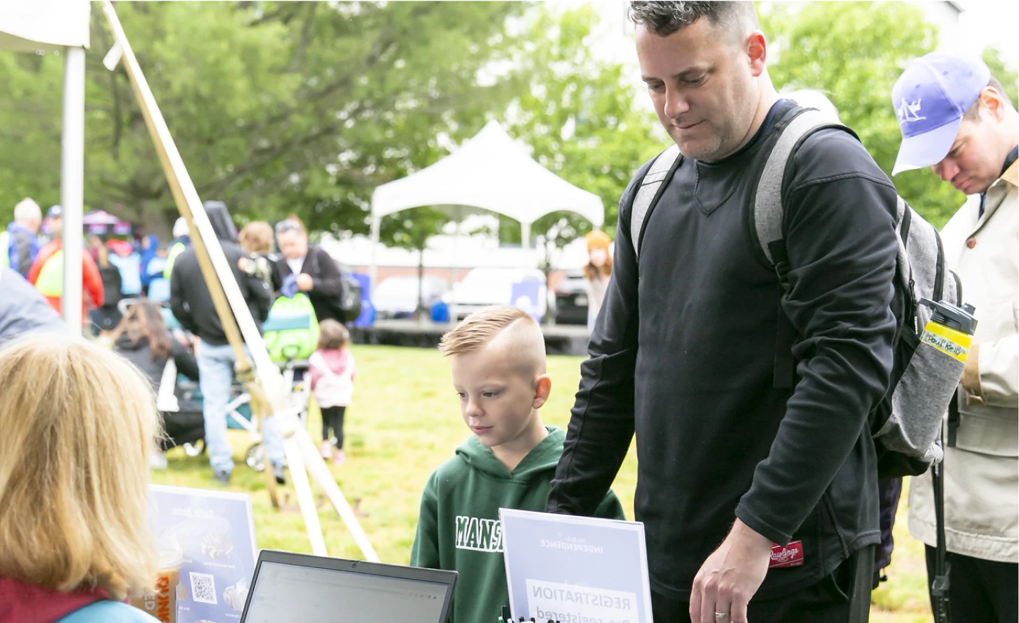 Father and young son check in at an outdoor registration booth during a community event