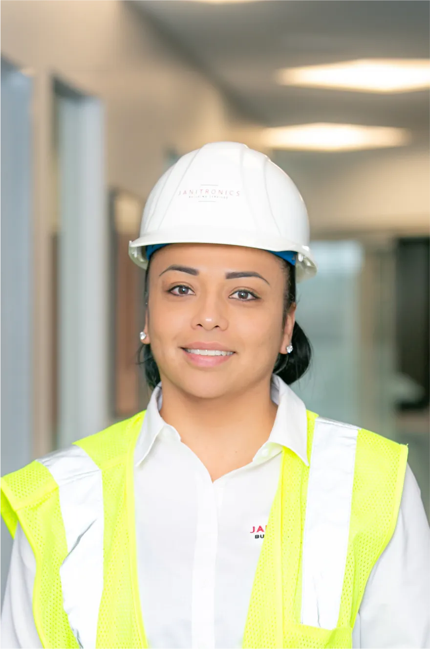 Female construction worker wearing a hard hat and safety vest smiling inside a modern office building