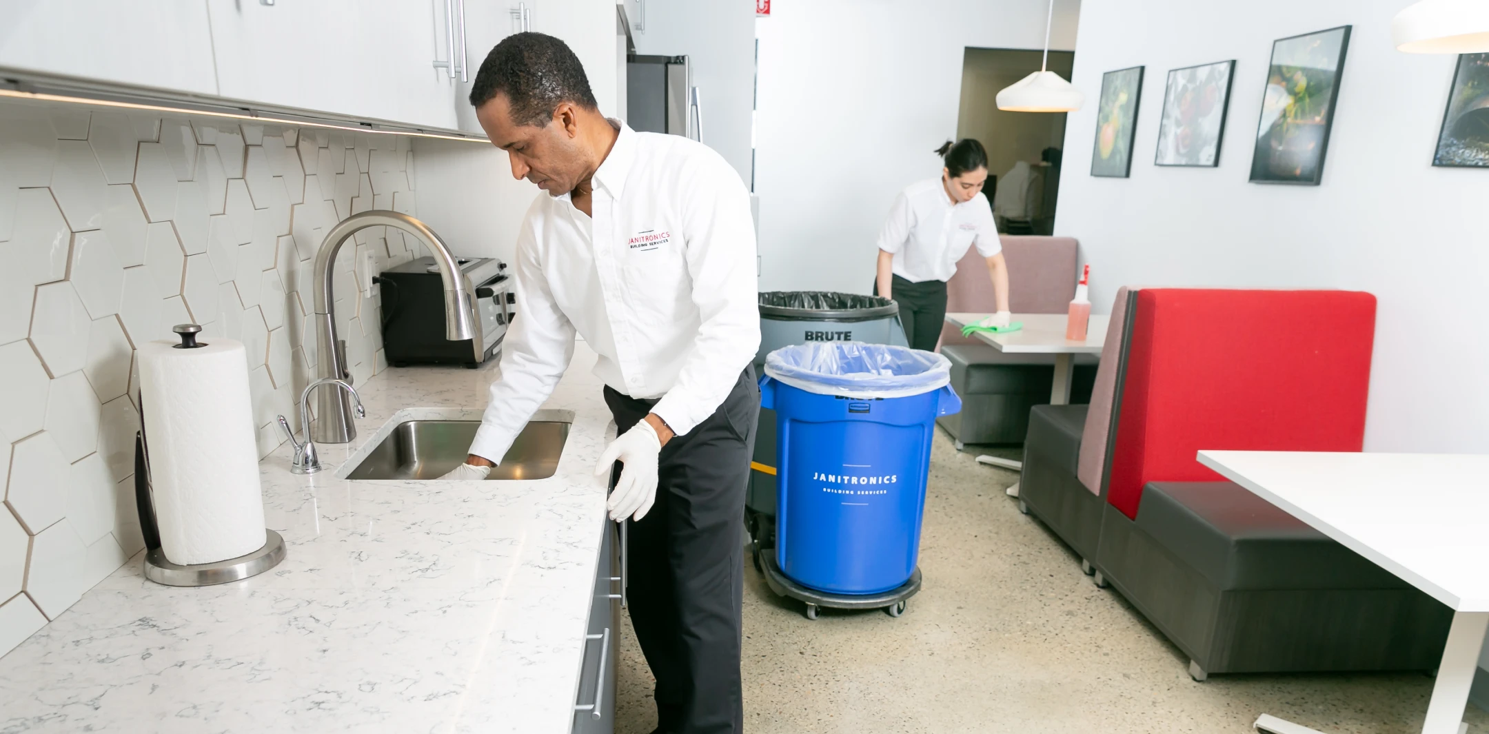 Janitorial staff cleans an office kitchen, wiping counters and sanitizing dining tables