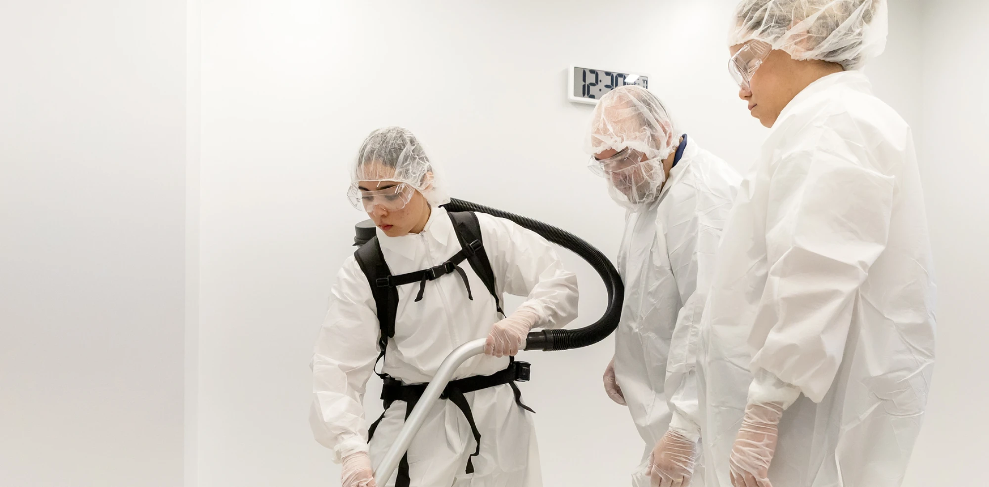 Workers in full protective suits clean a sterile environment using specialized vacuum equipment