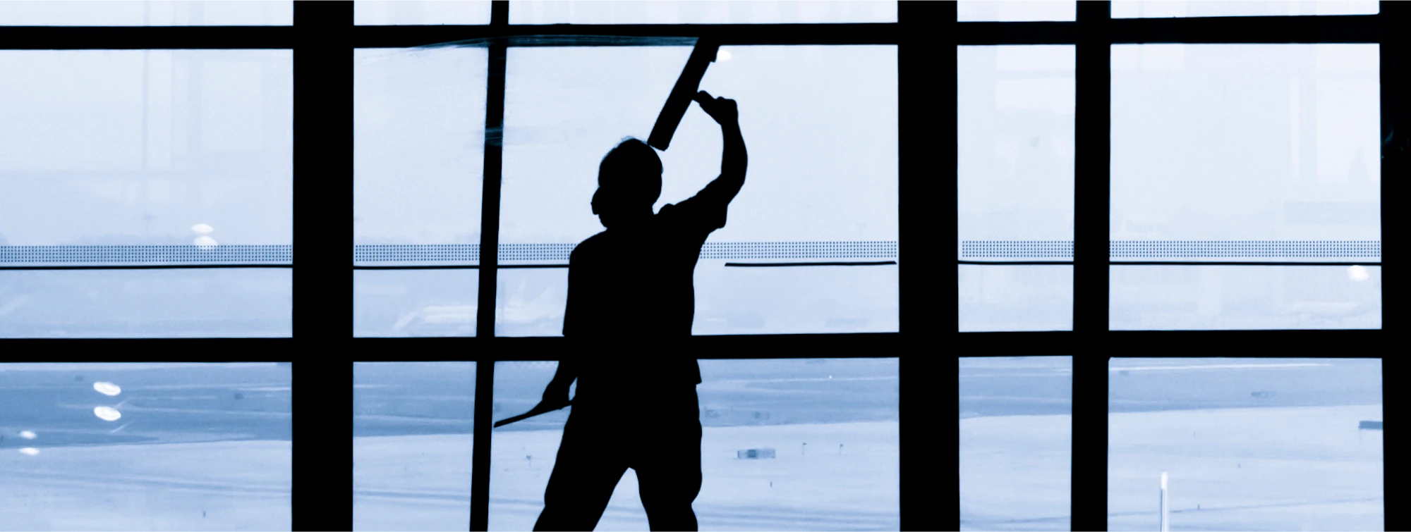 Silhouette of a window cleaner using a squeegee on large glass panels in a modern building