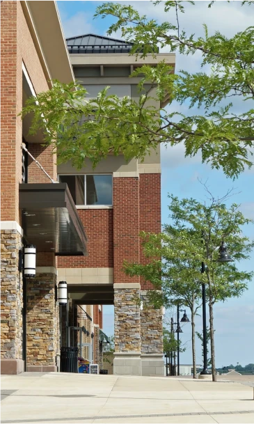 Modern commercial building with storefronts, brick columns, and sidewalk greenery