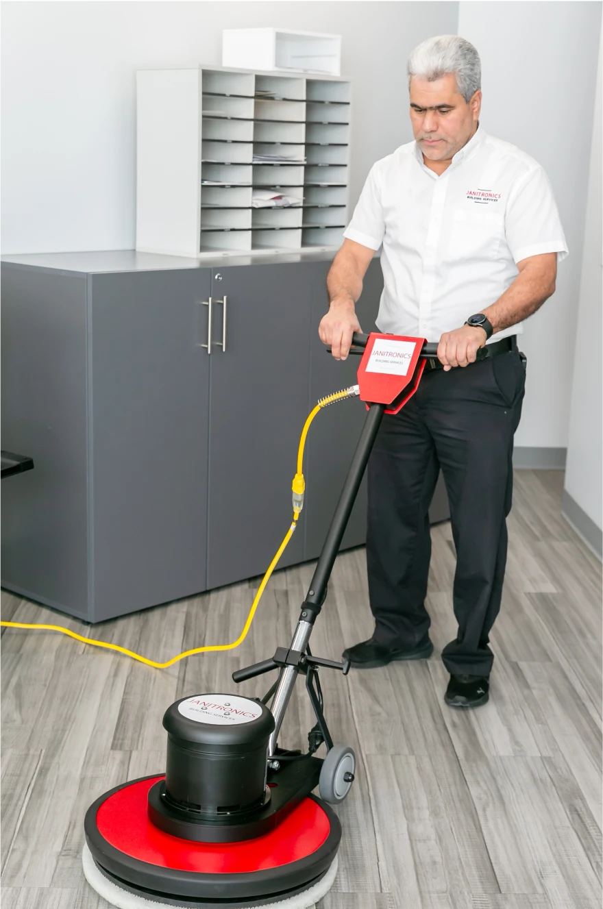 Janitorial worker using a floor buffer to maintain a clean and polished office space