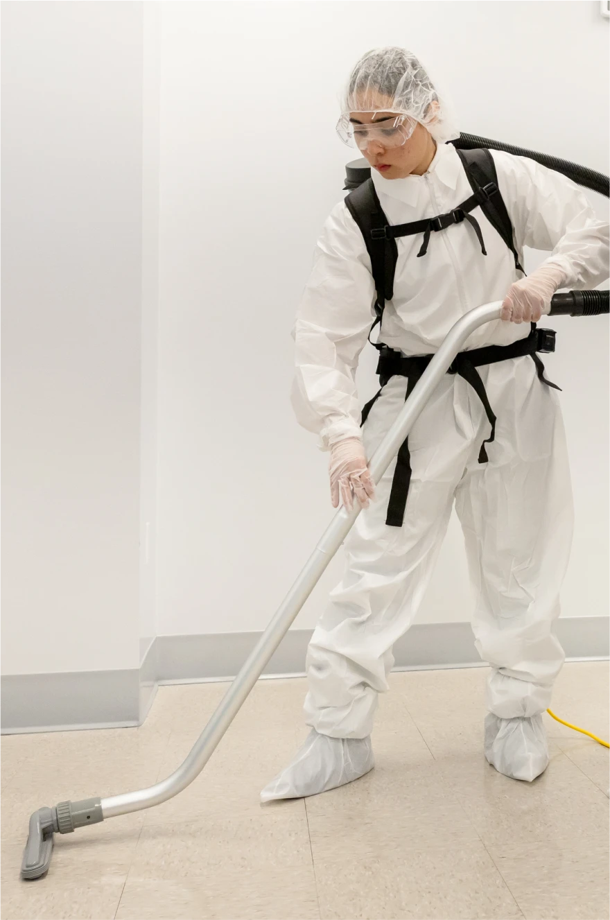 Cleaning technician in protective gear vacuuming a sterile laboratory environment