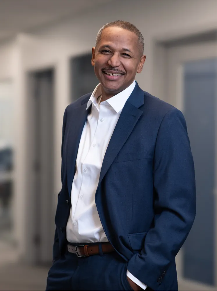 Smiling executive in a navy blue suit posing with hands in pockets in an office hallway