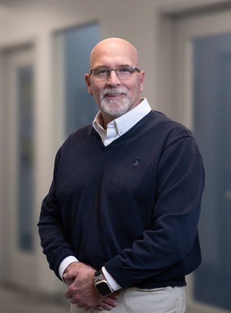 Corporate portrait of bald man in v-neck sweater and collared shirt in office setting