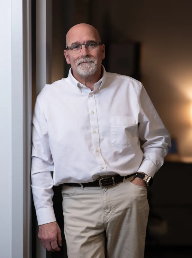 usinessman in a white dress shirt leaning casually against a doorframe in a dimly lit office
