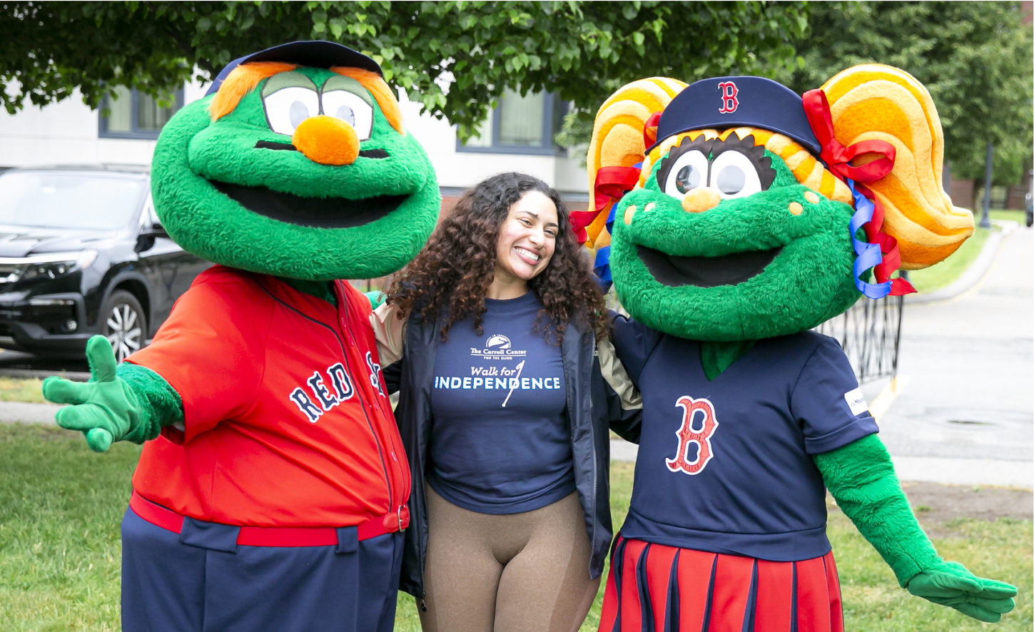 Woman in a Walk for Independence shirt poses with two Red Sox mascots at an event