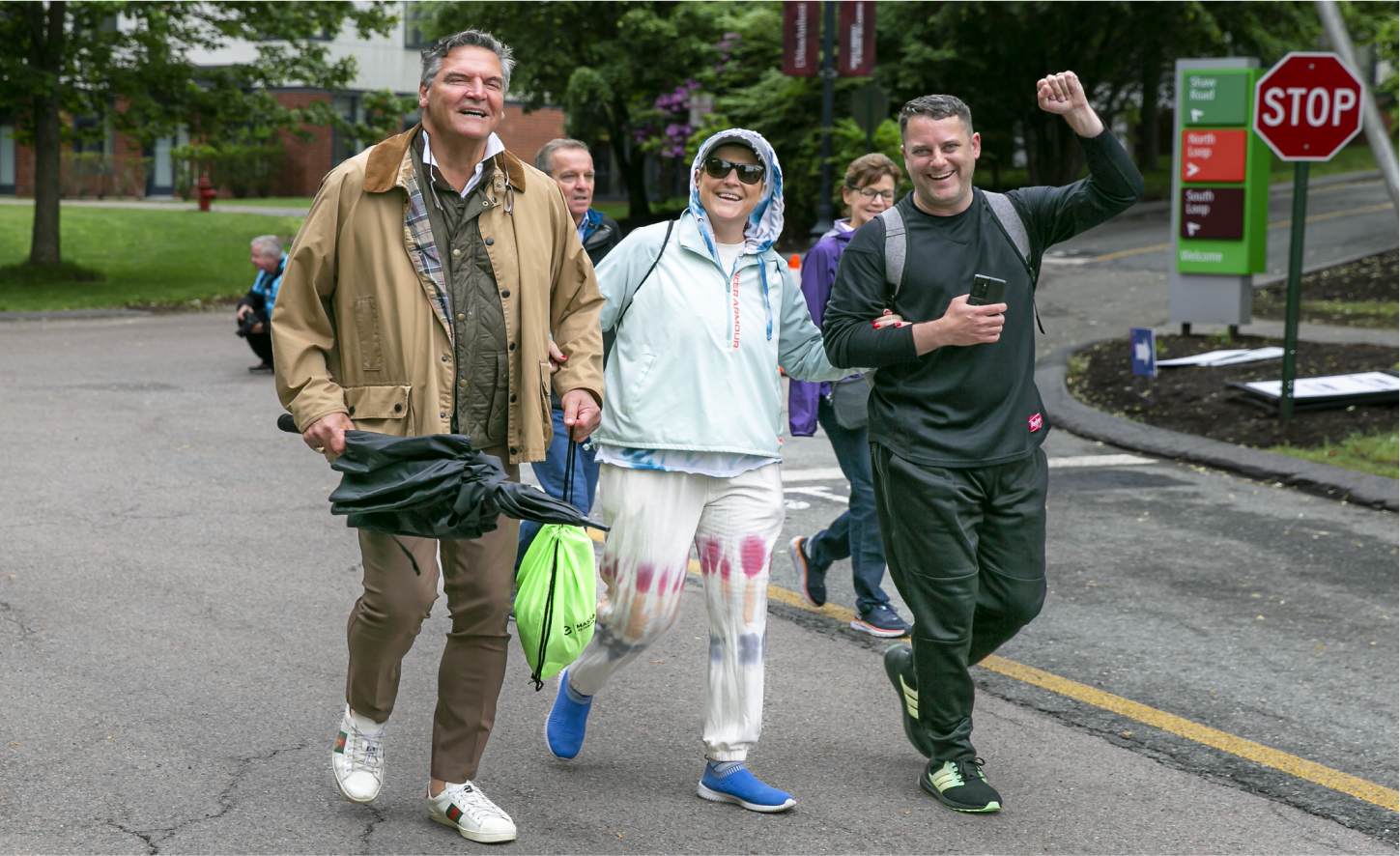 Three cheerful individuals walking arm-in-arm on a street during a public gathering