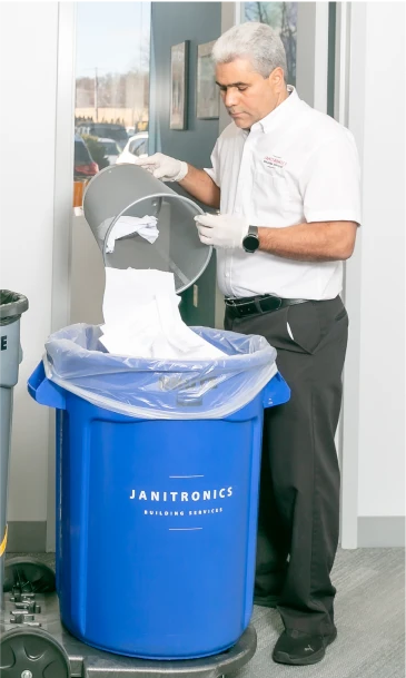 Cleaning professional emptying a trash bin into a branded Janitronics recycling container