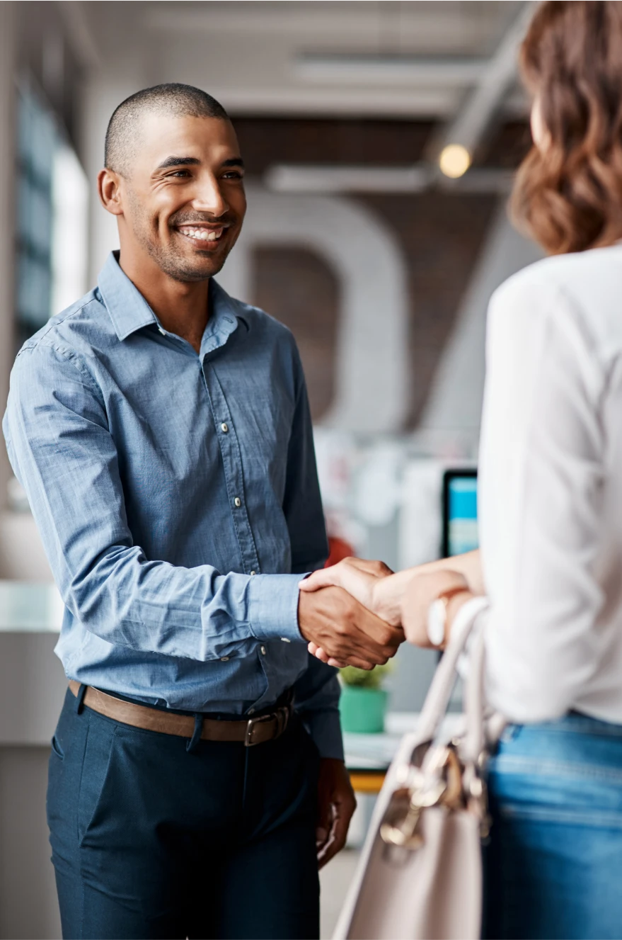 Smiling man in a blue shirt shakes hands with a woman in a professional office setting