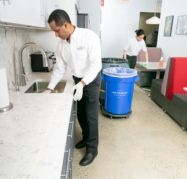 Janitronics employees cleaning a corporate breakroom, wiping down countertops and sanitizing tables