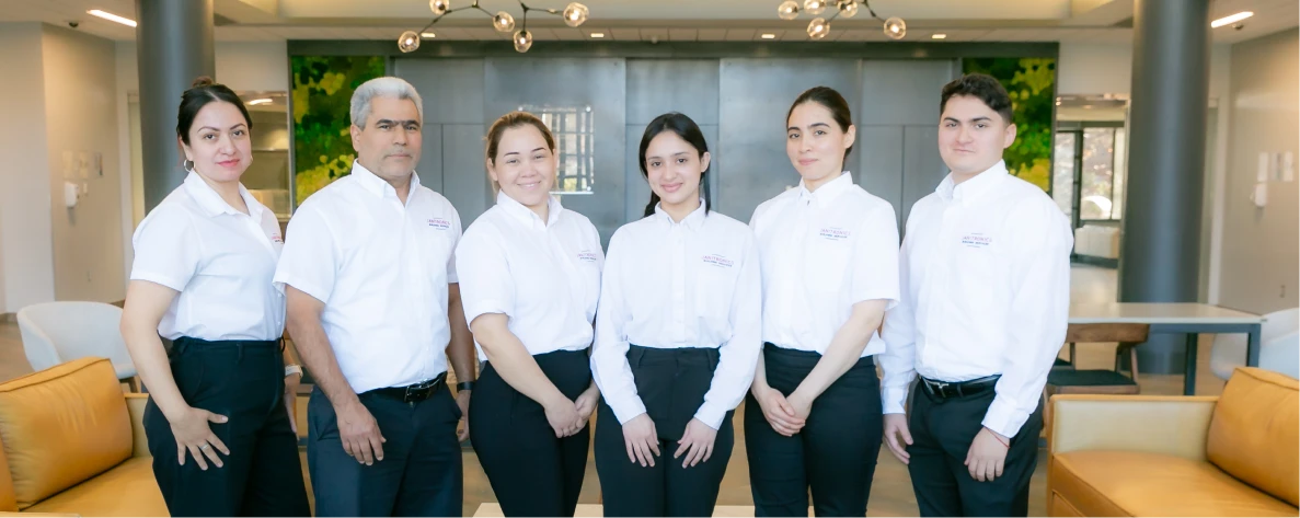 A group of six professionally dressed employees in white shirts posing in a modern office lobby