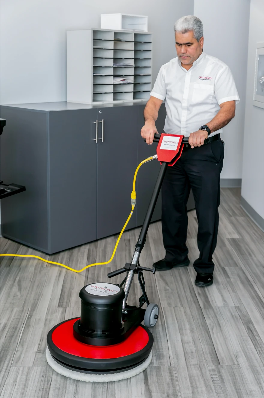 Janitorial worker operating a floor buffer machine to polish an office's wooden flooring
