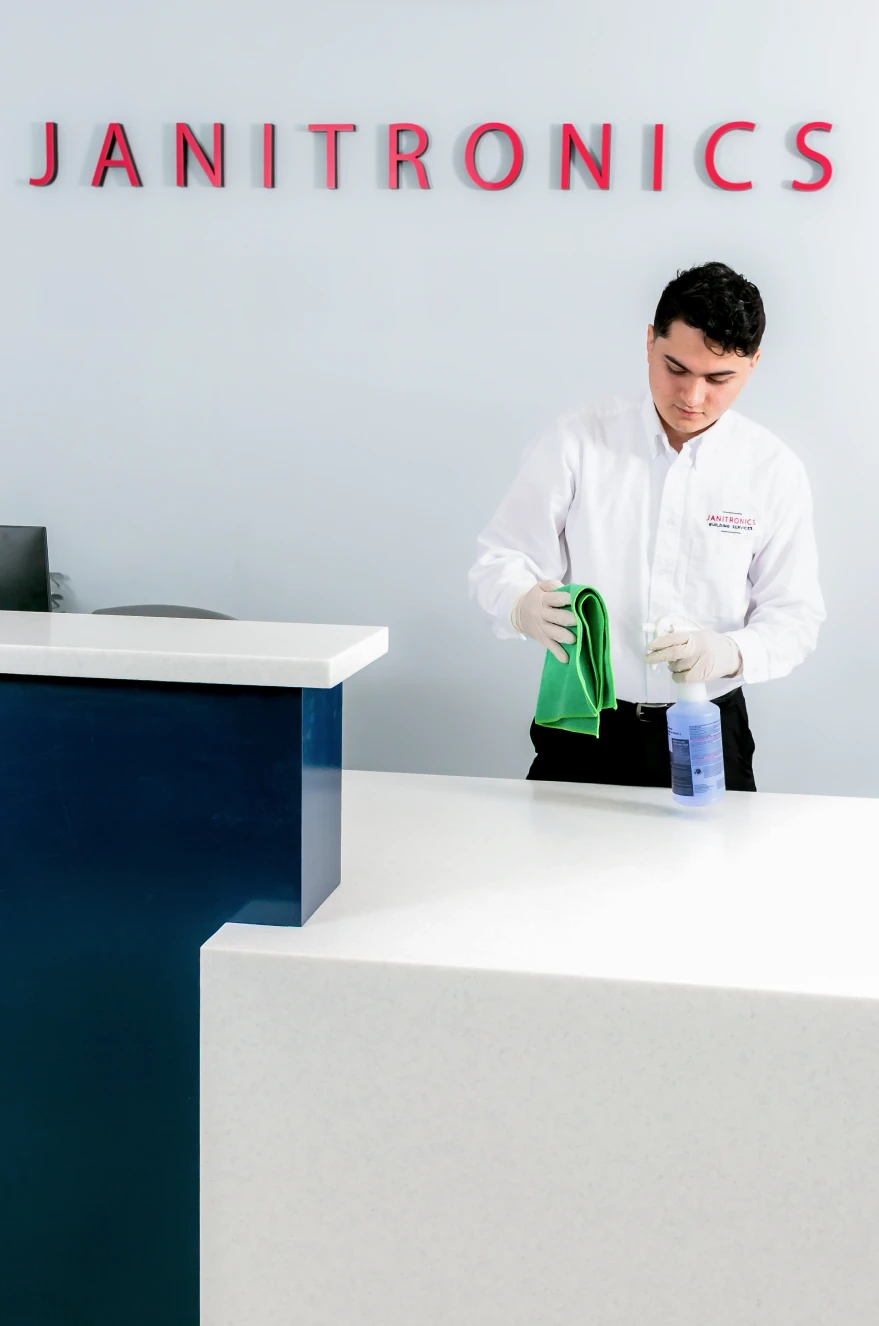 Cleaning staff member wiping down a white reception desk at Janitronics headquarters