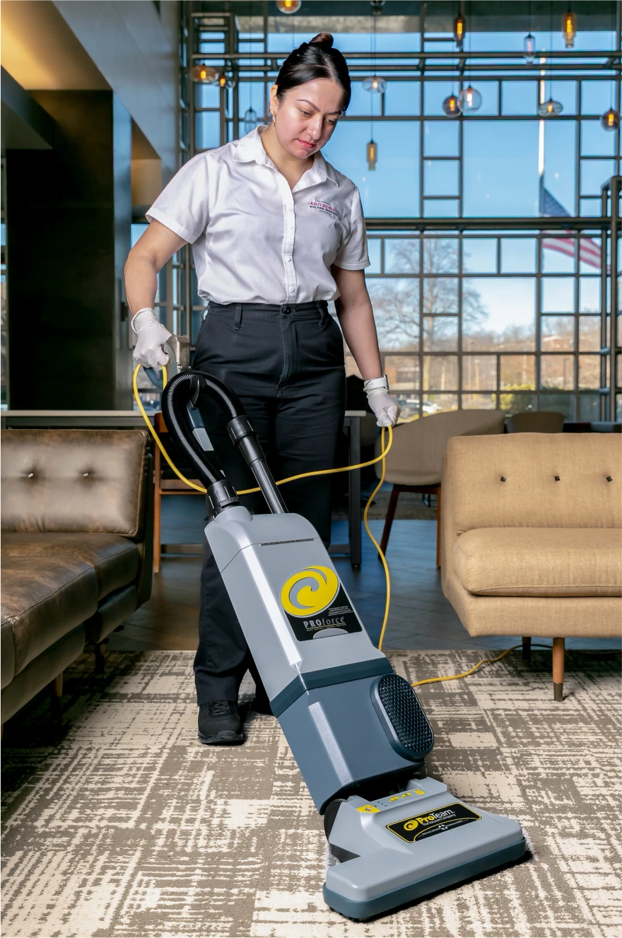 Janitorial worker in uniform deep cleaning an office carpet using an industrial vacuum cleaner