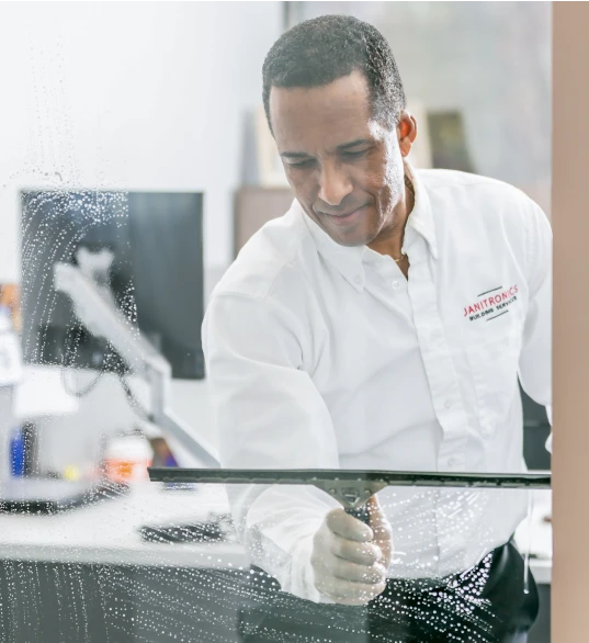 Janitronics employee smiling while using a squeegee to clean an office glass window