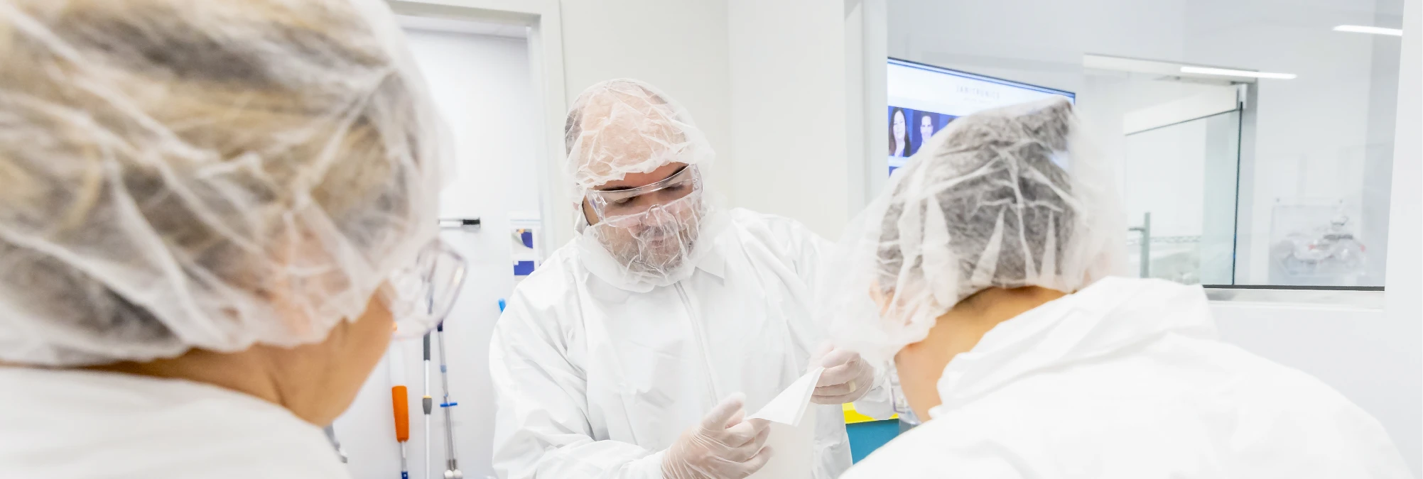 Laboratory technicians wearing white hazmat gear analyzing test samples in a controlled facility