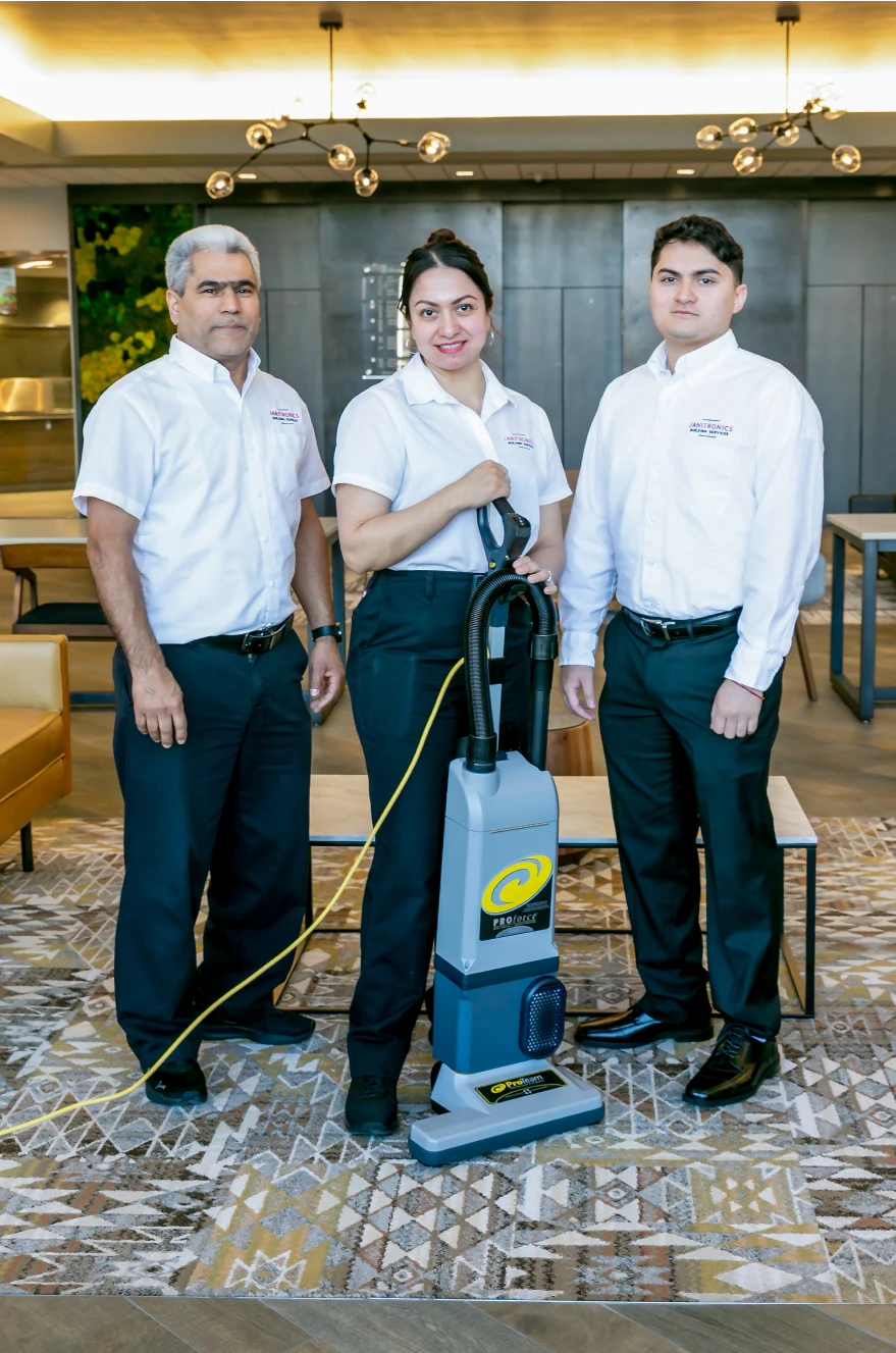 Three janitorial employees in uniform standing together with a professional cleaning machine